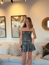 Vestido corto con estampado de rayas horizontales en tonos grises y negros. Diseño con escote halter que se ata al cuello, abertura central en el busto y falda corta con volado.