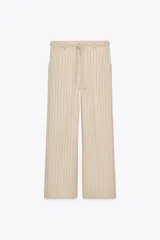 Pantalón de tiro alto color beige con finas rayas verticales negras, pernera ancha y cinturón trenzado a tono.
