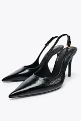 Zapato de tacón negro con efecto relieve en el cuerpo, tira trasera con hebilla ajustable, tacón fino y acabado en punta.