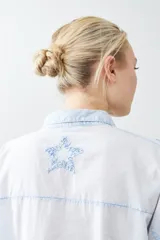 Camisa fucsia de manga larga con cuello camisero y cierre frontal con botones. Presenta apliques de estrellas bordadas en el frente y en el cuello.
