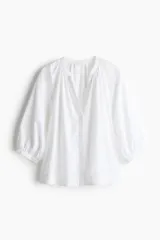 Blusa blanca de popelina de algodón con cuello mao, abertura en V y botones frontales. Mangas globo tres cuartos de corte raglán con puños finos y bajo recto.