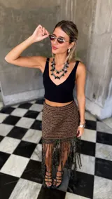 Falda corta tejida a mano en crochet, con diseño a rayas horizontales en tonos marrón oscuro y dorado brillante. Presenta un borde inferior con flecos largos y abundantes.