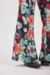 Pantalón palazzo de tela fluida con estampado floral en tonos naranja, celeste y blanco sobre fondo negro.