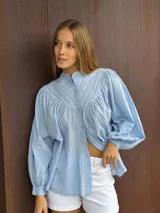 Camisa blanca de algodón con cuello mao, mangas largas abullonadas y cierre frontal con botones.