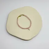 Pulsera elástica con cuentas de cuarzo rosa y dije de cruz dorada con incrustaciones brillantes.