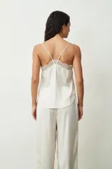 Blusa color crudo con lunares dorados, breteles finos y escote en V con detalle de encaje.