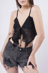 Top corto color rosa pálido, estilo camisola con tirantes finos y escote en V con lazo ajustable al frente. Presenta textura de encaje o tejido calado con pequeños detalles florales y volados en el ruedo.