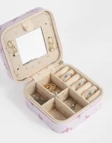 Caja cuadrada porta bijou color lila con estampado de moños rosas y cierre perimetral con cremallera.