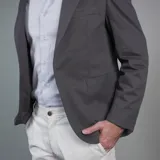 Saco color beige de gabardina, con solapas de muesca, cierre de dos botones, tres bolsillos externos y un bolsillo interno.