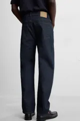 Jeans de corte slim fit confeccionados en denim de algodón sin lavados, color azul oscuro. Cierre frontal con botones y cinco bolsillos.