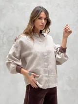 Camisa beige a rayas verticales finas, con cuello clásico, mangas largas abullonadas con puños marrones y cierre frontal con botones.