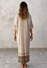 Vestido largo de tejido de punto color marrón topo, con cuello polo y cierre frontal de botones. Presenta detalles de rayas grises en las mangas y un bloque de color beige y gris en el ruedo. Tiene aberturas laterales.