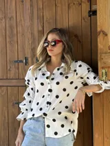 Camisa blanca con lunares negros, de corte holgado y mangas largas abullonadas con puños elásticos.