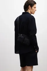 Camisa negra de sirsaca de algodón con cuello inglés, tapeta clásica, bolsillo superior de parche y canesú con pliegue de caja en la espalda. Mangas largas con tapeta de manga y botón, y cierre ajustable de botón en los puños. Bajo redondeado y corte holgado.