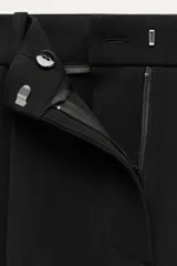 Pantalón negro de tiro alto con pinzas delanteras, pernera ancha y cinturón con hebilla dorada.