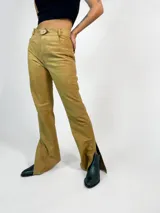 Pantalón de cuero color ocre, de corte jean con bota acampanada y abertura lateral en el ruedo. Tiene tiro medio-alto y cierre frontal con botón de madera.