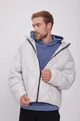 Campera puffer de hombre color gris claro, con capucha ajustable con cordón, cierre de cremallera frontal, bolsillos laterales y mangas largas. Tejido acolchado resistente al viento.