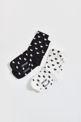 Pack de dos pares de medias de algodón, uno blanco con corazones negros y otro negro con corazones blancos.