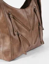 Cartera hobo color crudo de cuero sintético, con correa de hombro ajustable y múltiples cierres decorativos en el frente.
