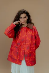 Campera tipo parka reversible con estampado de flores rojas y naranjas sobre fondo rojo, cuello marrón y bolsillos frontales.
