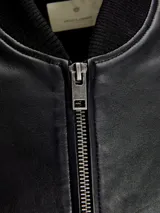 Campera bomber negra de cuero con cuello, puños y cintura acanalados. Cierre frontal con cremallera y bolsillos laterales con botón a presión.