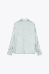Camisa celeste de tejido satinado, con cuello solapa, manga larga con puños y cierre frontal con botones.