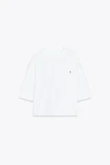 Camiseta blanca de algodón, corte oversize, cuello redondo, manga corta y detalle de aplique metálico con logo ZA en el frente.
