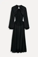 Vestido midi negro de cuello redondo y manga larga abullonada con puños. Tiene cintura elástica y detalle de espalda descubierta. El cierre es con botón en el cuello.