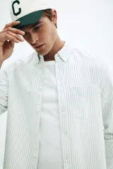 Camisa de manga larga color blanco roto con finas rayas verticales en tono oscuro. Presenta cuello americano, bolsillo superior abierto y corte estándar.