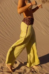 Pantalón de lino color amarillo, de corte ancho y tiro medio. Presenta detalles de estampa con motivos geométricos en la cintura y laterales.