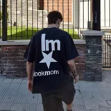 Camiseta negra con efecto acid wash, corte oversize y estampado trasero blanco con el texto "lm" sobre una estrella y el texto "lookmom" debajo.