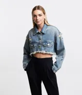 Campera cropped de jean celeste con cuello solapa, cierre frontal con botones, mangas largas, barra deshilachada con flecos y detalles de roturas.