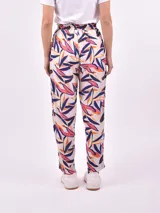 Pantalón babucha de tela estampada con hojas en tonos rosa, naranja y azul, con cintura elastizada y lazo para ajustar.