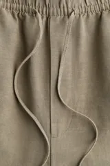 Pantalón tobillero color beige de corte holgado en tejido liviano de mezcla de lino. Modelo de tiro alto con elástico revestido y cordón para ajustar fino en la cintura, bolsillos al bies y piernas ajustadas.
