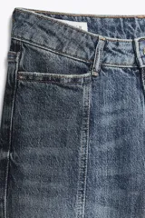 Pantalón de jean azul de tiro alto con nervio marcado delantero, bolsillos delanteros y traseros, bajo acampanado y cierre frontal con cremallera y botón.