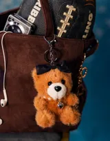 Llavero con dije de oso de peluche color marrón claro, con moño negro, collar de perlas y dije de corazón plateado.