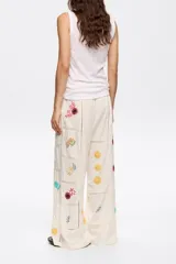 Pantalón de corte recto color crema con bordados florales multicolores.