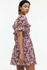 Vestido corto color lila con estampado floral en blanco, escote cuadrado con volados, mangas cortas abullonadas con elástico y cuerpo fruncido.