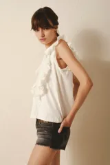 Remera negra sin mangas con volados en los hombros y escote en V. Incluye un collar largo de cuentas con un nudo decorativo. Jeans de tiro bajo.