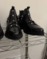 Botines negros de cuero vacuno, de caña baja con elástico lateral y detalle de arneses con hebillas y tachas plateadas.