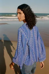 Camisa azul con bordados blancos, de cuello redondo con escote pico y manga larga.