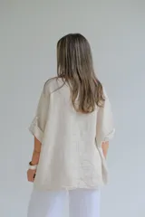 Blusa beige de lino con mangas 3/4 y apliques de tela estampada con motivos florales en bolsillo y parte inferior.