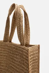 Bolso tipo shopper color marrón claro, con acabado trenzado. Tiene un compartimento principal con cierre de imán y un bolsillo plano interior. Cuenta con dos asas de mano.
