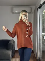 Sweater de punto color borgoña, con cuello alto y mangas largas. Decorado con strass en el frente.