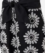 Pantalón zanahoria de cintura alta, confeccionado en laise negro con bordado floral blanco y lazo en la cintura.