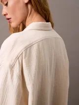 Camisa color crema de gasa doble, con cuello de punta, bolsillo de parche en el pecho, mangas largas con cierre de solapa enrollable y corte regular.