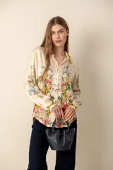 Blusa color crema con estampado floral y detalles de diseño barroco, con cuello mao, mangas 3/4 y cierre frontal con botones.
