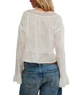 Blusa blanca de manga larga, confeccionada en algodón con bordados florales y detalles de encaje en el escote y mangas. Presenta un escote en V con botones frontales y un cordón ajustable en el bajo para fruncir.