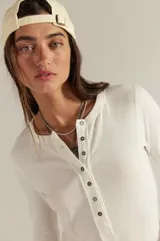 Camiseta tipo henley de manga larga, color blanco, confeccionada en algodón elástico con cuello redondo y tapeta de botones.