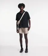 Camisa negra de sarga, corte boxy, con cuello inglés, manga corta, abotonadura frontal y bolsillo en el pecho.